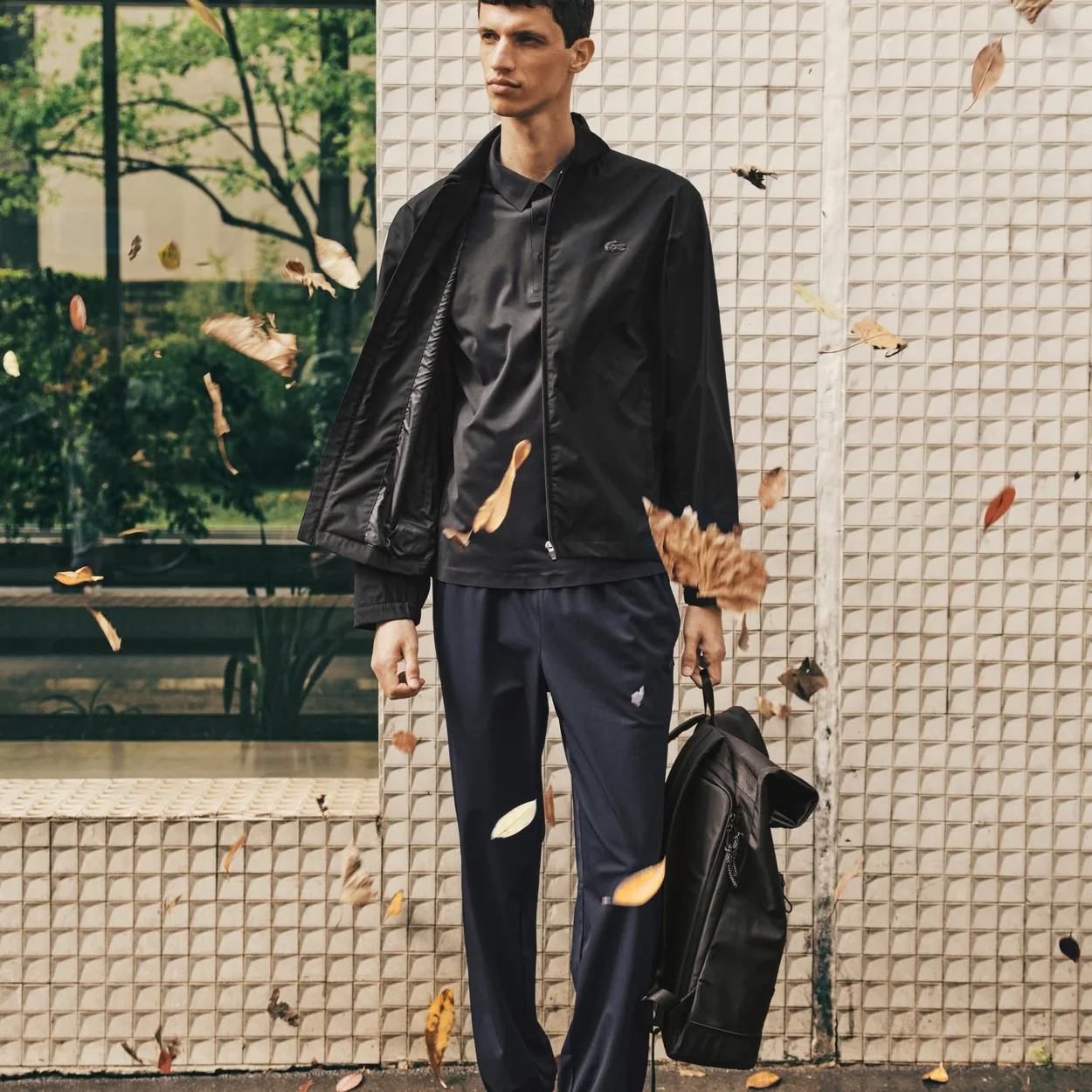 Hombre con chaqueta y pantalon negros de Lacoste en la calle